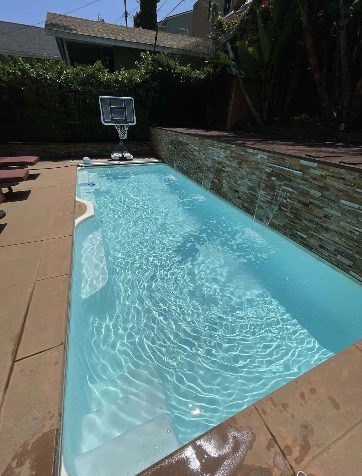 Sunlit residential pool with waterfall feature and blue water